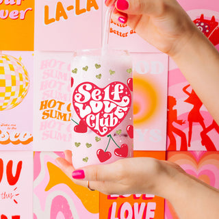 Wholesale 20oz glass cups with bamboo lid and glass straw featuring red hearts and gold glitter for self love gifts.
Women’s empowerment wholesale gifts with Self Love Club 20oz glass cups, bamboo lid, and glass straw.