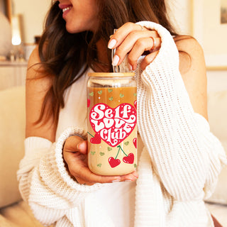 Wholesale 20oz glass cups with bamboo lid and glass straw featuring Self Love Club design, red heart, and cherry graphics.
Self Love Club 20oz glass cups with bamboo lid, glass straw, and gold glitter hearts for an empowering Valentine’s gift.