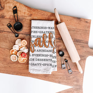 fall words towel used as backdrop for thanksgiving desserts
autumn text dish towel with black fonts and bold script
fall kitchen cloth featuring list of seasonal comforts
autumn cozy sayings towel beside copper cookware
