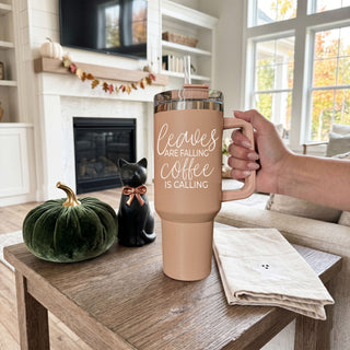 Stay cozy all season long with this stylish 40oz fall tumbler featuring the phrase “Leaves Are Falling, Coffee Is Calling” in a trendy neutral aesthetic design. This insulated stainless steel handled tumbler keeps drinks hot or cold for hours and includes a reusable straw with spill-resistant lid.